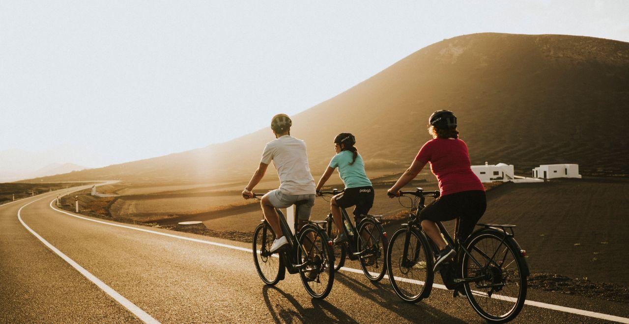Cyclists riding on a road with rolling hills and white buildings at sunset.