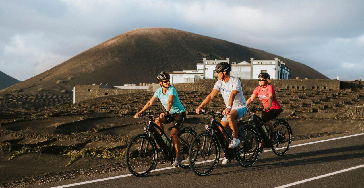 Cyclists riding on a road with a volcanic landscape in the background.
