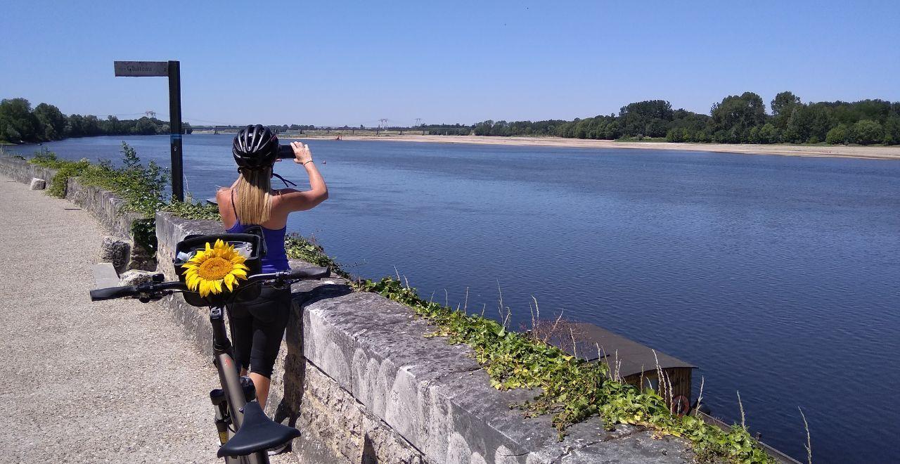 Cyclist with a sunflower on her bike, taking photos by a river.