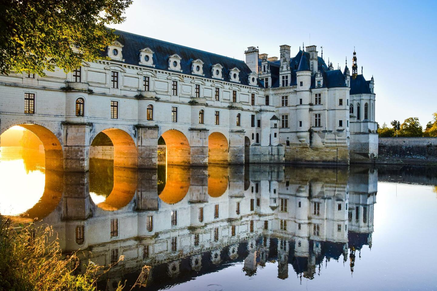 Majestic Château de Chenonceau spanning river, sunset reflections, iconic French castle and heritage site.