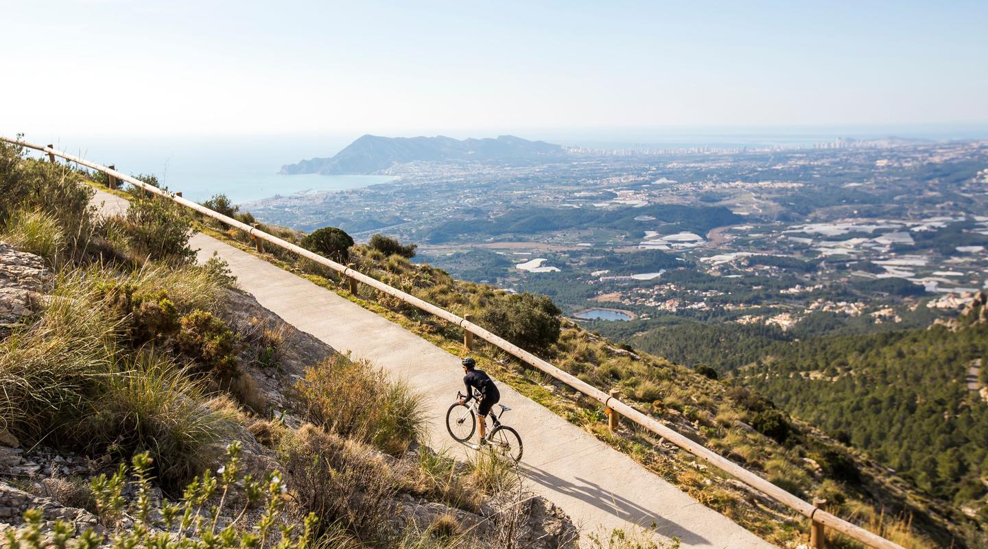 “A cyclist riding on a hill overlooking a sprawling cityscape and coastline with mountains in the background in Calpe, Costa Blanca.”