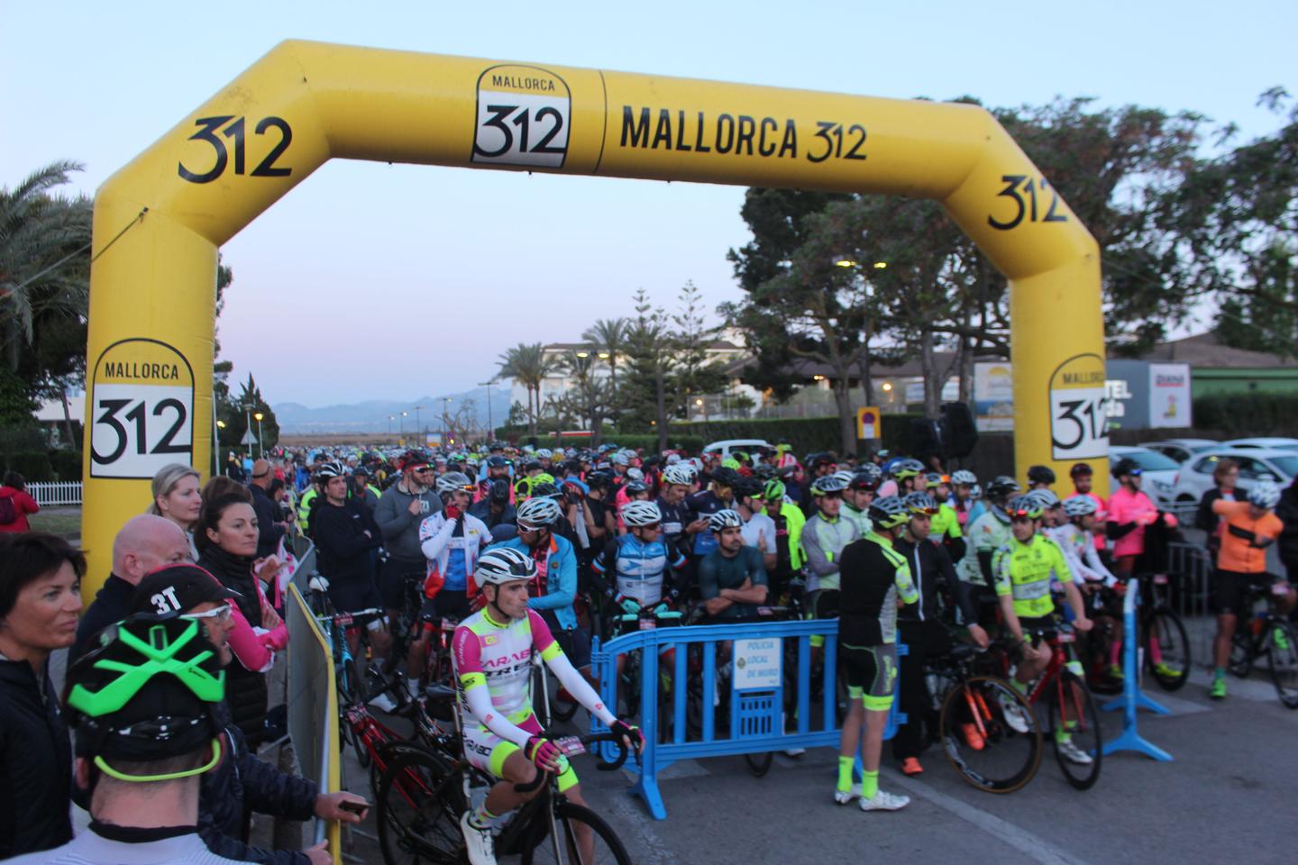 Cyclists gather at the start line of the Mallorca 312 event under the iconic yellow arch.
