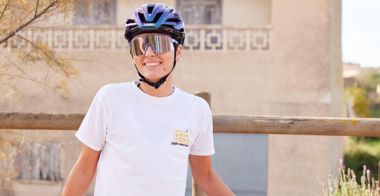 Woman in a white shirt and helmet standing with her bike, smiling.