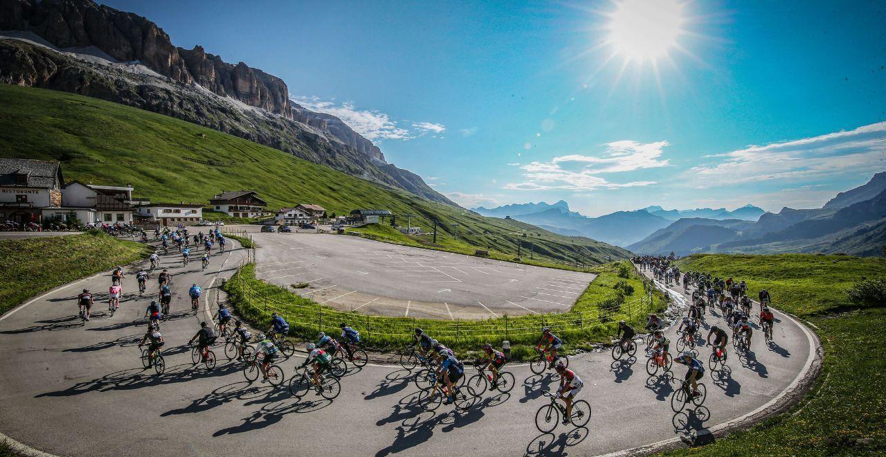 Cyclists rounding a mountain curve under a bright sun.