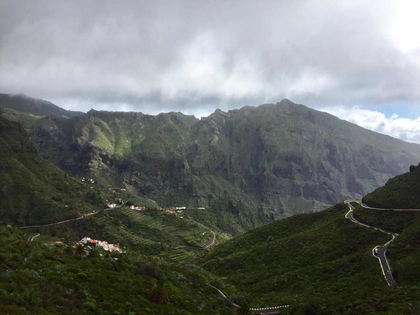 View of the Masca Valley in Tenerife, featuring winding roads that snake through lush green mountains under a cloudy sky.