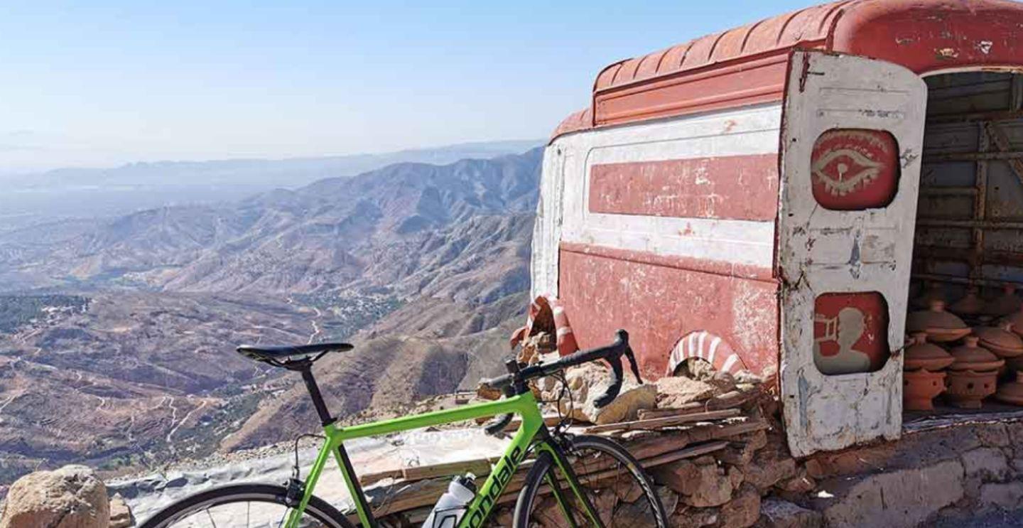 Green road bike leaning against an old, red and white vehicle overlooking a vast mountainous landscape.