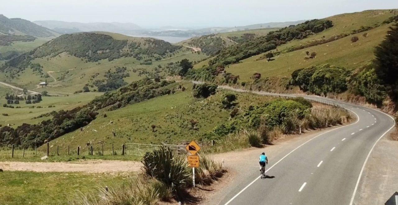 Lone cyclist on a winding road through green hills on the Alps 2 Ocean Cycle Trail.