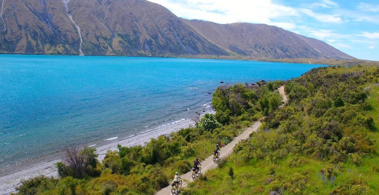 Cyclists riding along the turquoise waters of Lake Pukaki on the Alps 2 Ocean Cycle Trail.