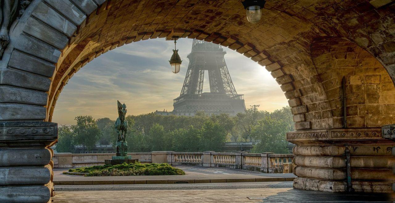 View of the bottom half of the Eiffel Tower through a stone arch bridge with statue in the foreground
