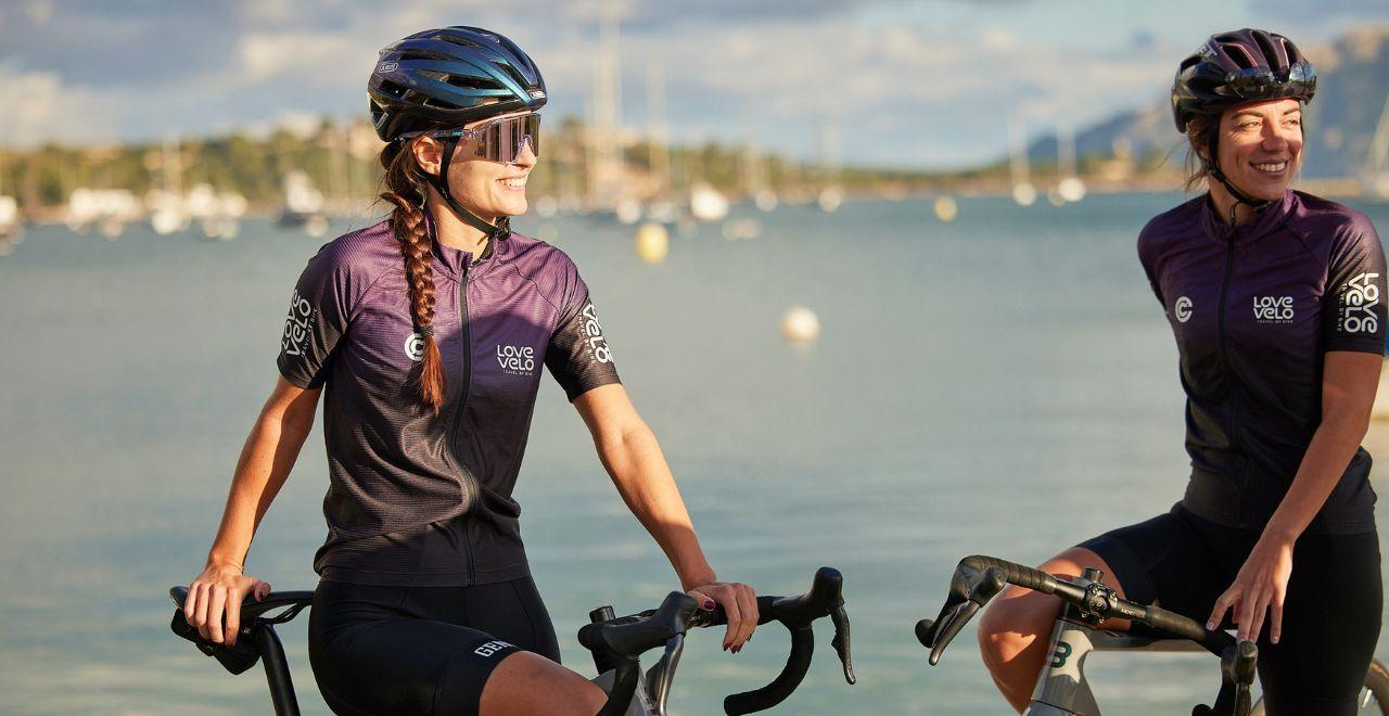 Two female cyclists smiling while taking a break by the sea.
