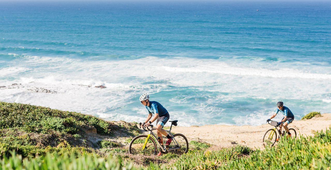 Two cyclists riding along a coastal cliff with ocean view