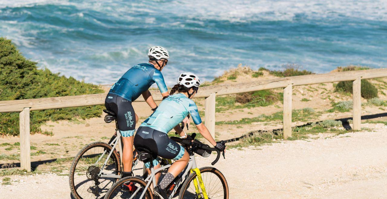 Two cyclists riding by the ocean on a dirt path