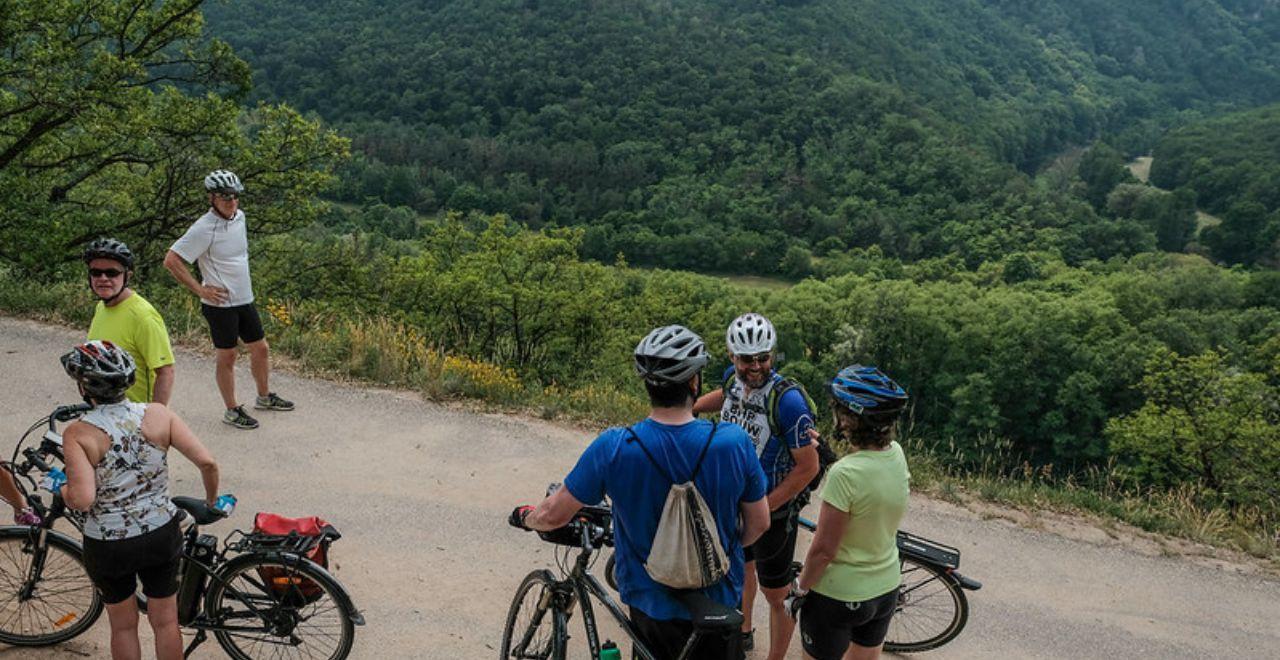 Group of cyclists stopping for a break on a hill with a forested valley in the background.