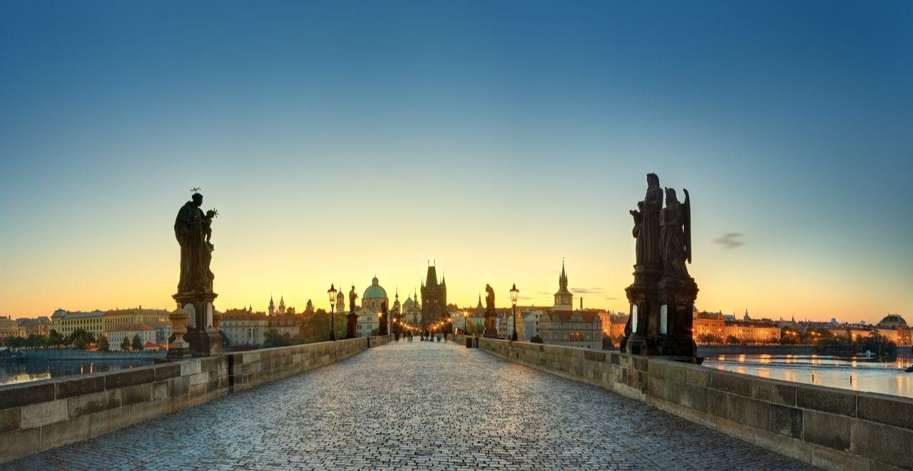 Charles Bridge in Prague at dawn with statues and historical buildings in the background.