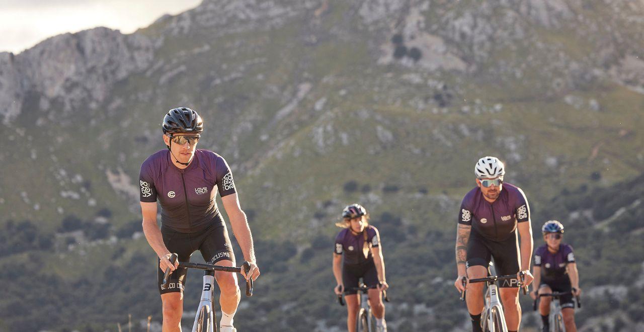Close-up of cyclists in purple jerseys riding on a mountain road with rocky hills in the background