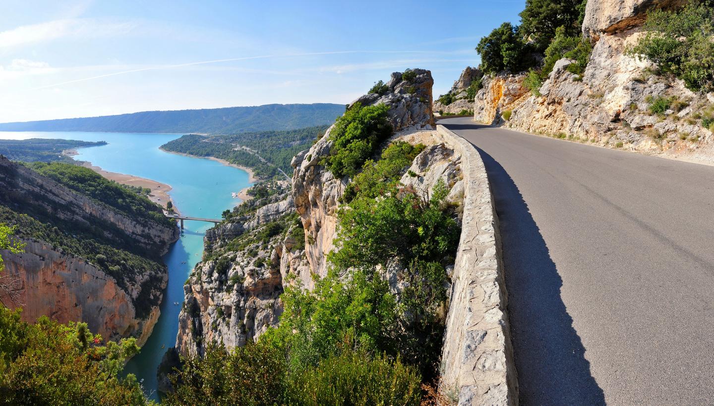 A scenic road winding along the edge of Gorges du Verdon with turquoise waters and lush greenery below.