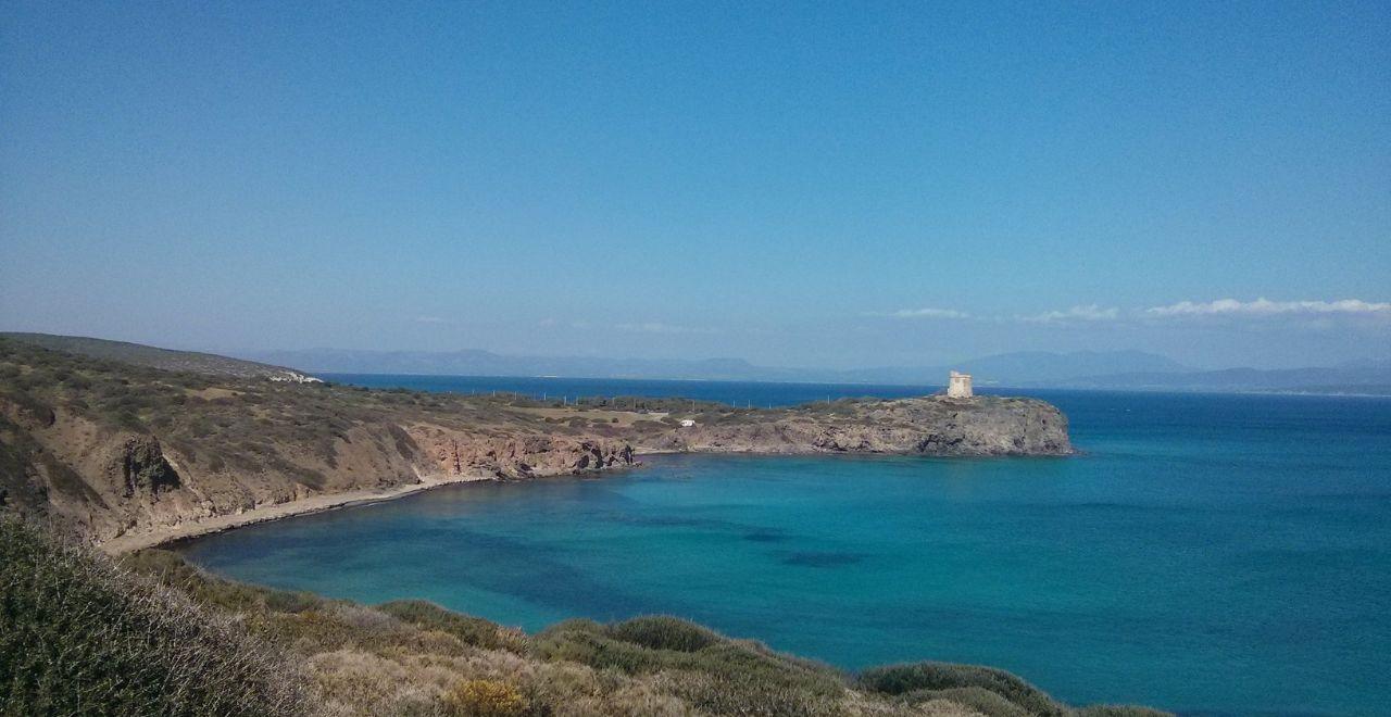 Coastal view with turquoise waters and a small tower on a rocky cliff.