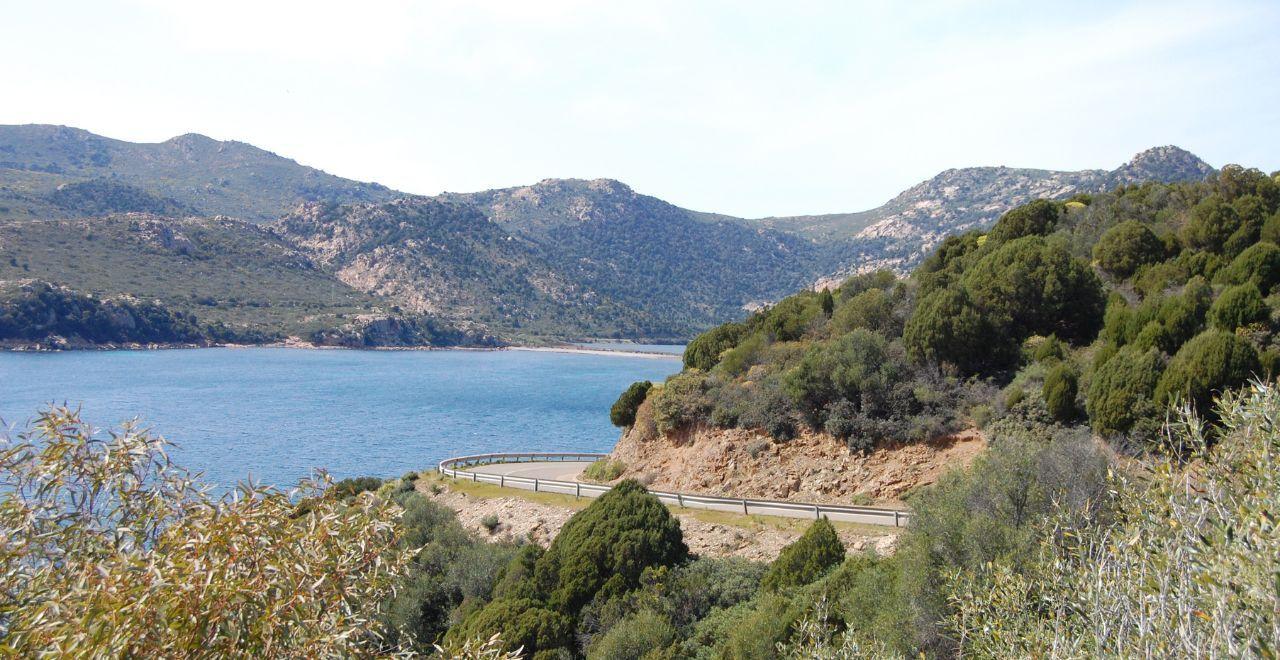 Scenic coastal road winding along a blue lake with mountainous backdrop.
