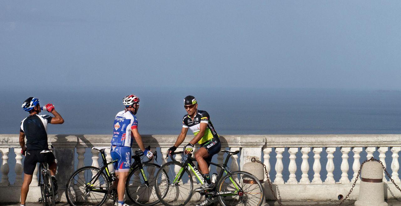 Three cyclists resting by a balustrade overlooking the sea.