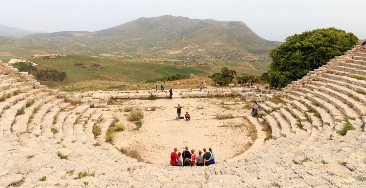 Tourists exploring an ancient stone amphitheater with panoramic countryside views.