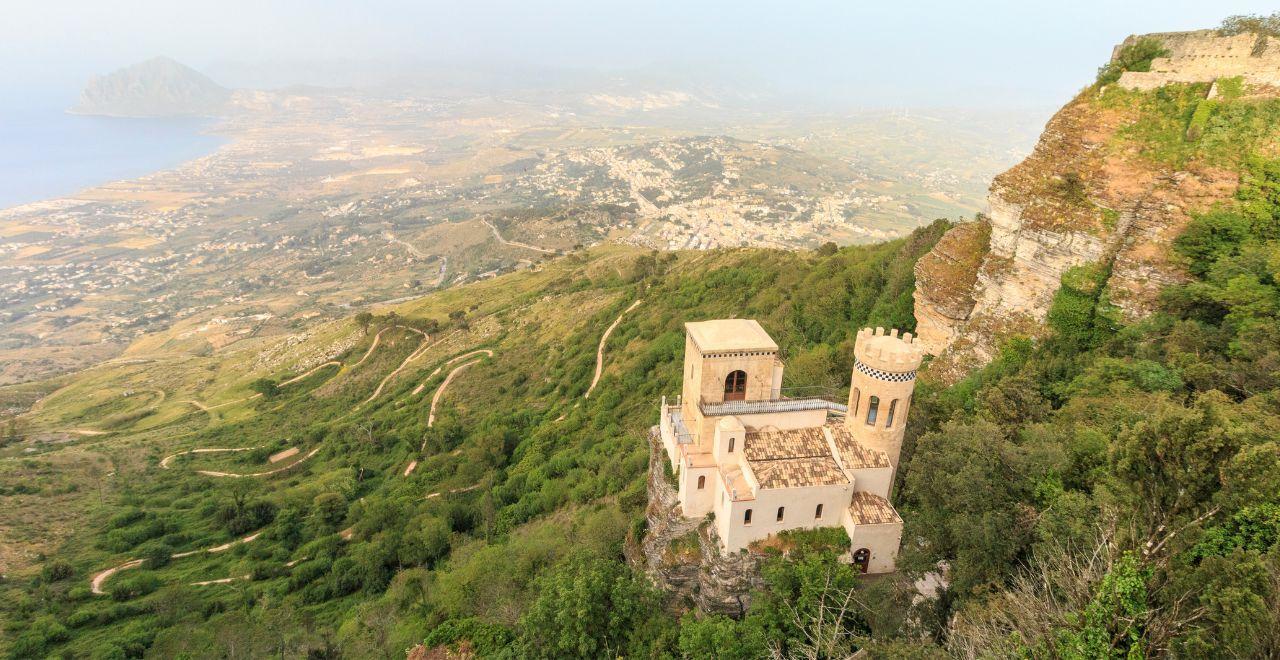 Aerial view of a historic castle on a hillside with a vast landscape below.