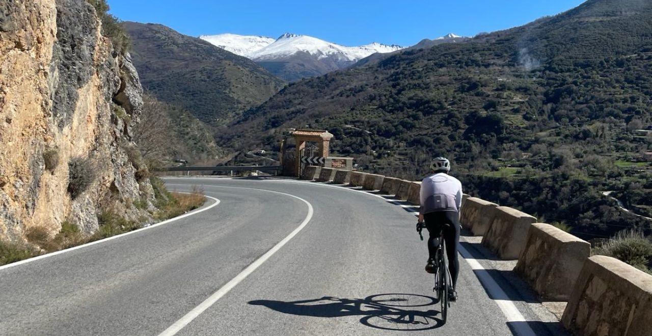 Cyclist riding along a winding mountain road with snow-capped peaks in the distance.