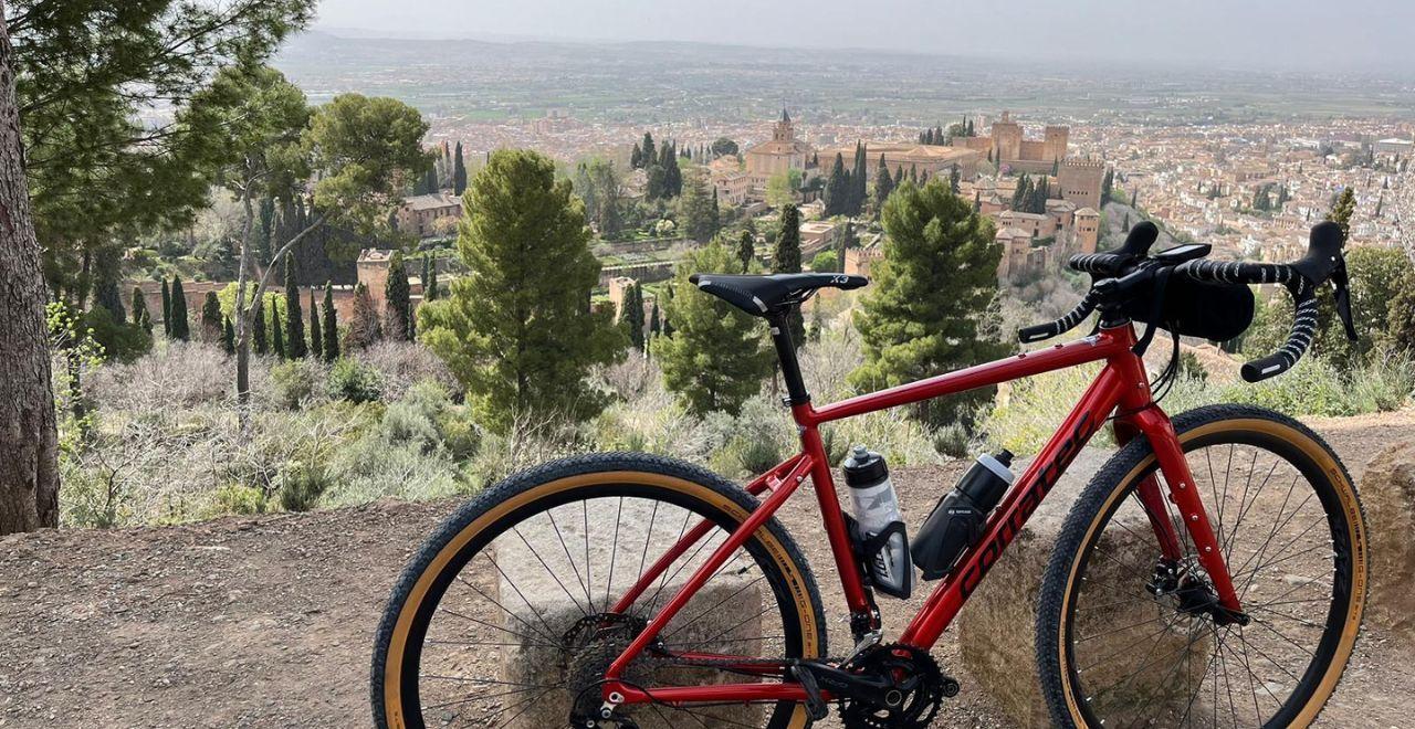 Red bike overlooking Alhambra in Granada with lush greenery and cityscape in the background.