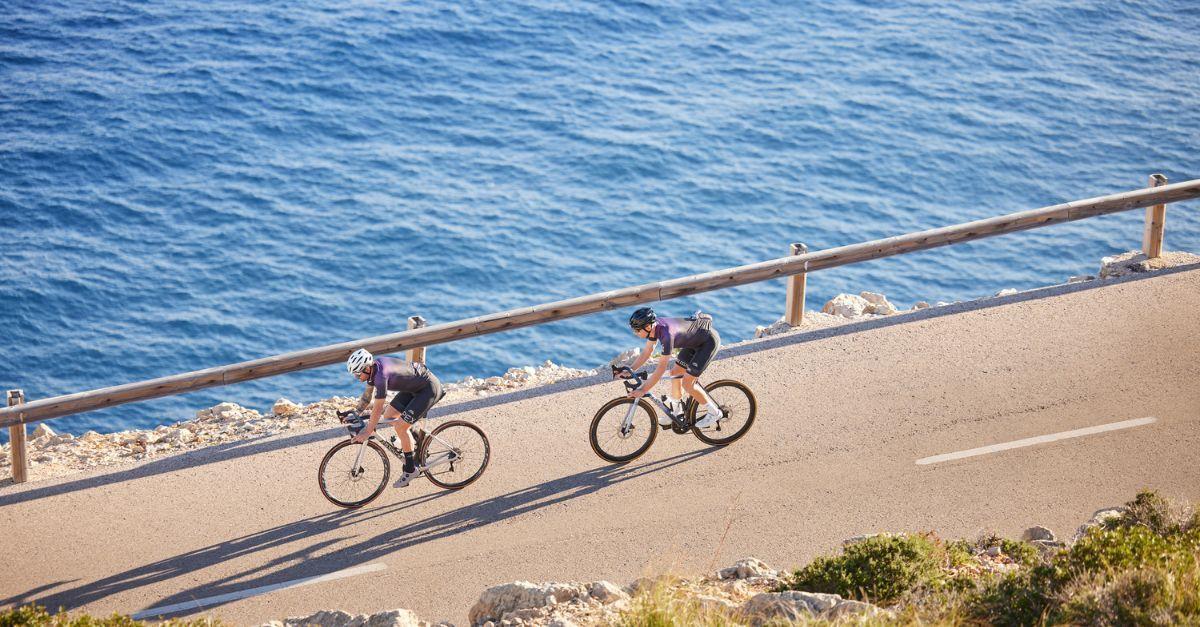 Cyclists riding on a coastal bike path next to a steep cliff with expansive views of the blue ocean.