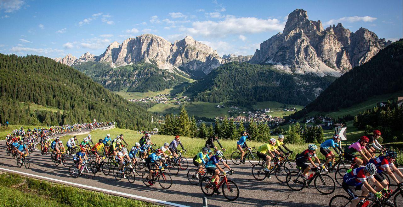 Large group of cyclists participating in the Maratona dles Dolomites, riding through scenic mountain landscape with towering peaks.