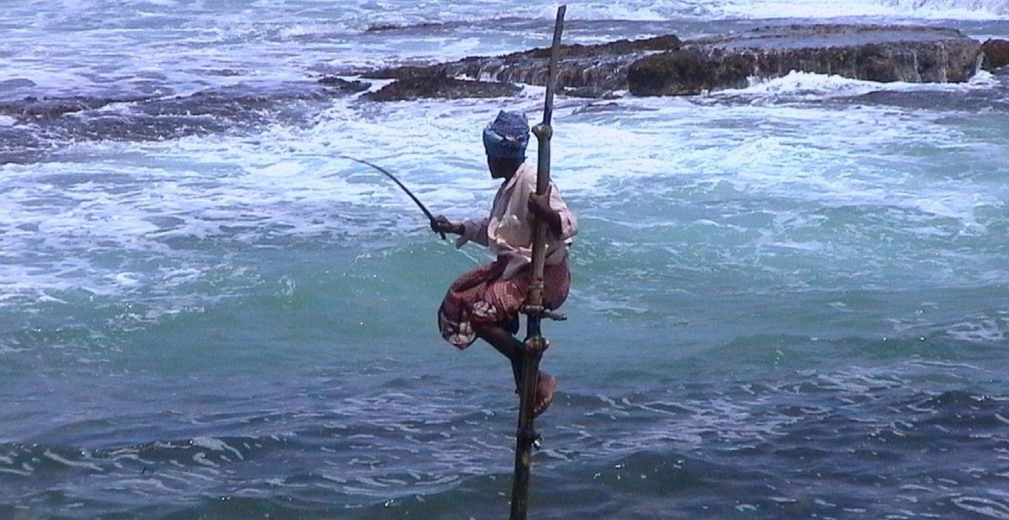 Traditional stilt fisherman balancing on a pole in the ocean waves