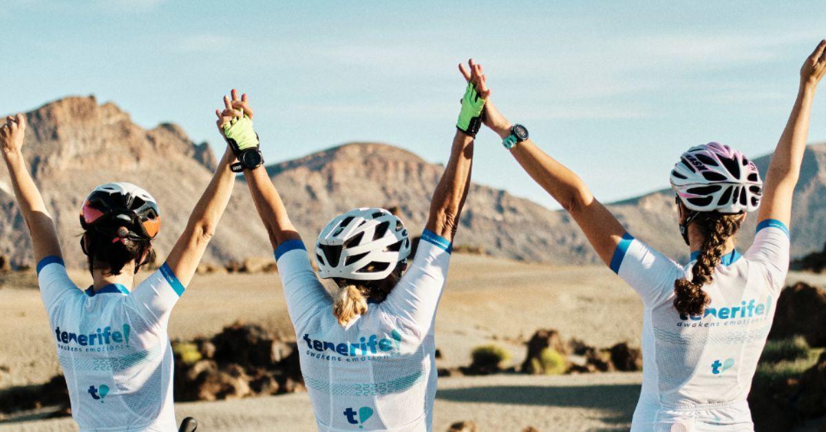 Three cyclists celebrating with raised hands against a backdrop of striking volcanic landscape under a clear sky.