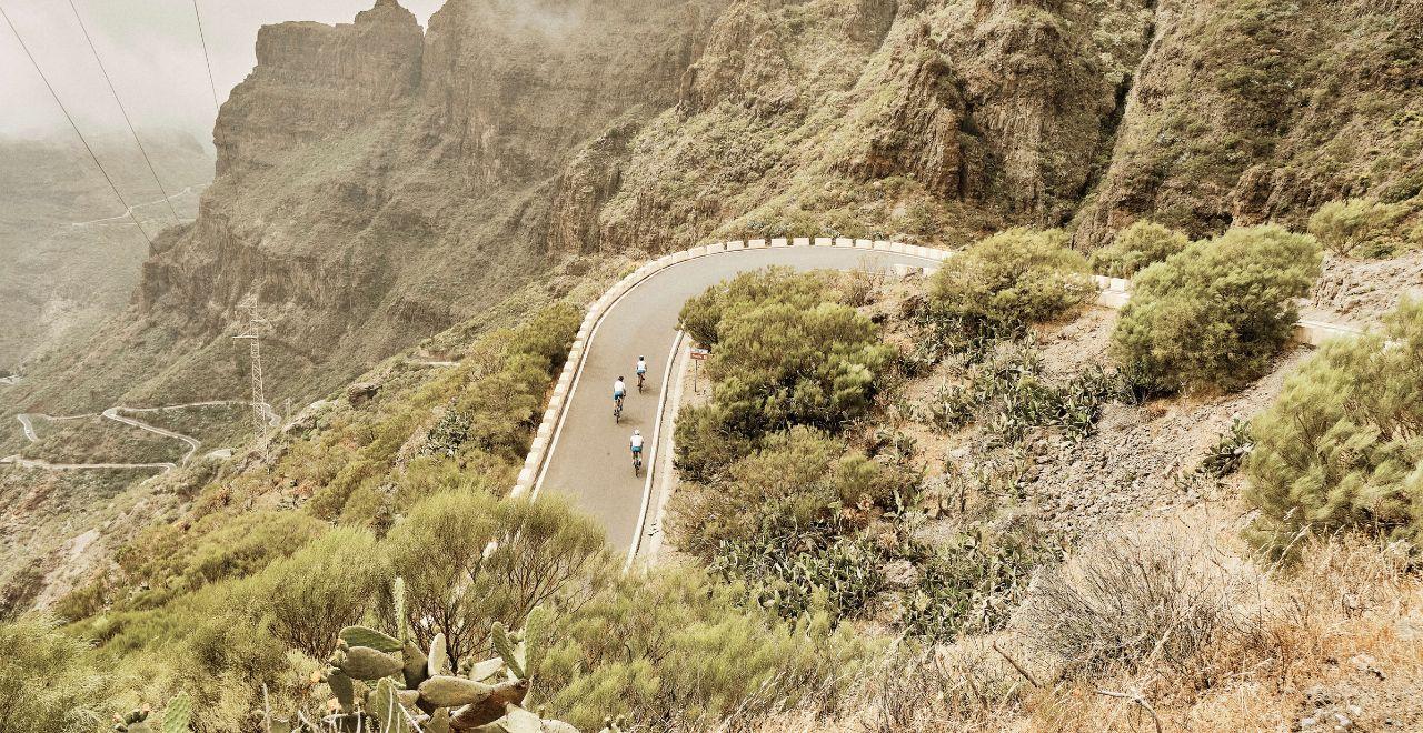 Cyclists navigating a winding road in Masca, Tenerife, with breathtaking views of the mountainous landscape.