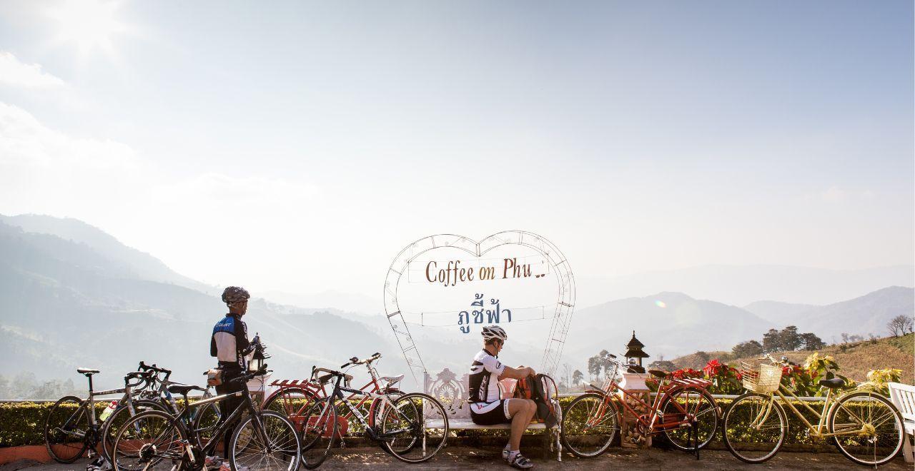 Cyclists resting at "Coffee on Phu" viewpoint with mountain backdrop