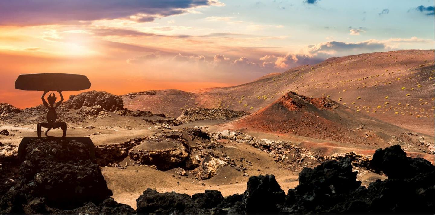 Sunset over the volcanic landscape of Timanfaya National Park in Lanzarote, with the park's iconic demon sculpture silhouetted against the colorful sky.
