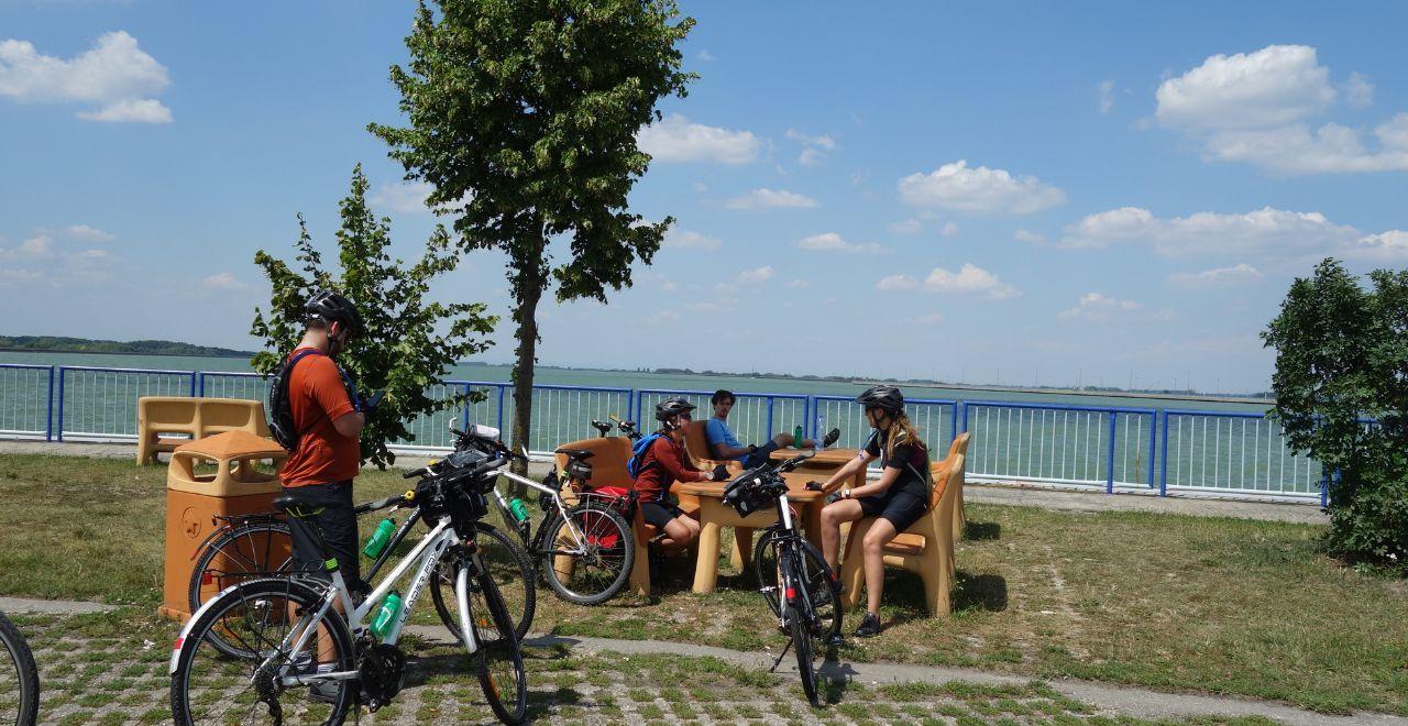 Cyclists taking a break at a picnic area with tables and benches by a lakeside