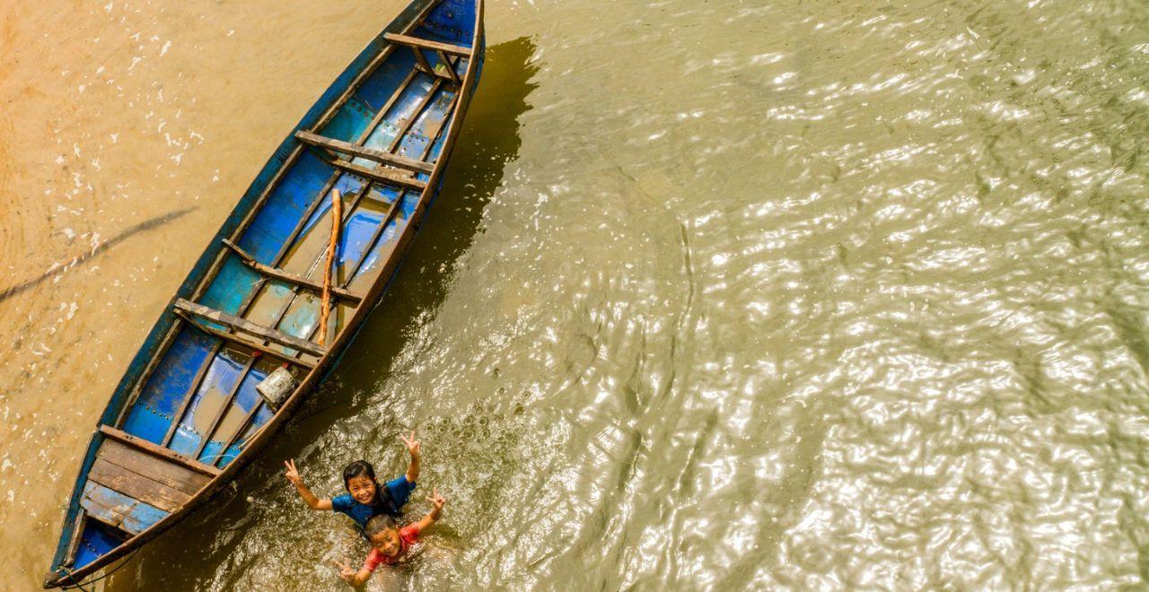 Joyful children waving from a rustic boat on a river in Vietnam, capturing the local charm during a cycling tour