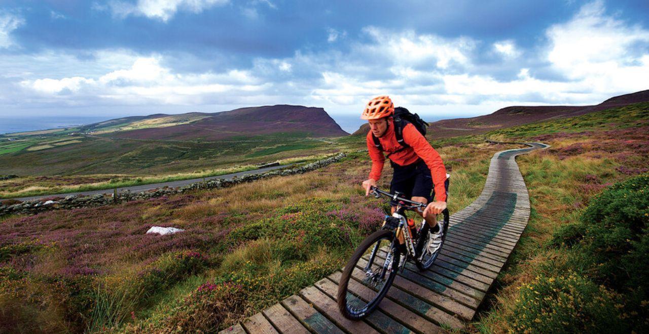 Cyclist in orange jacket riding on a scenic trail with mountains in the background