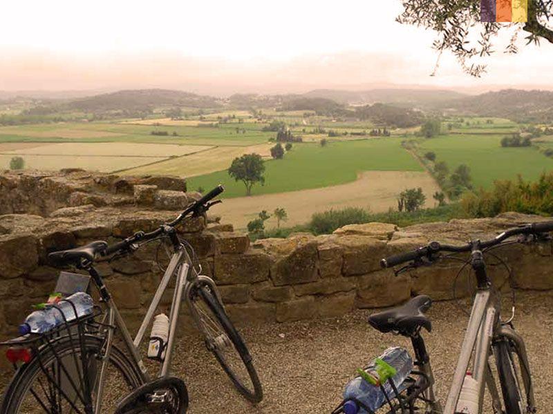 Three bicycles parked on a stone wall overlooking a vast, green agricultural landscape under a hazy sky.