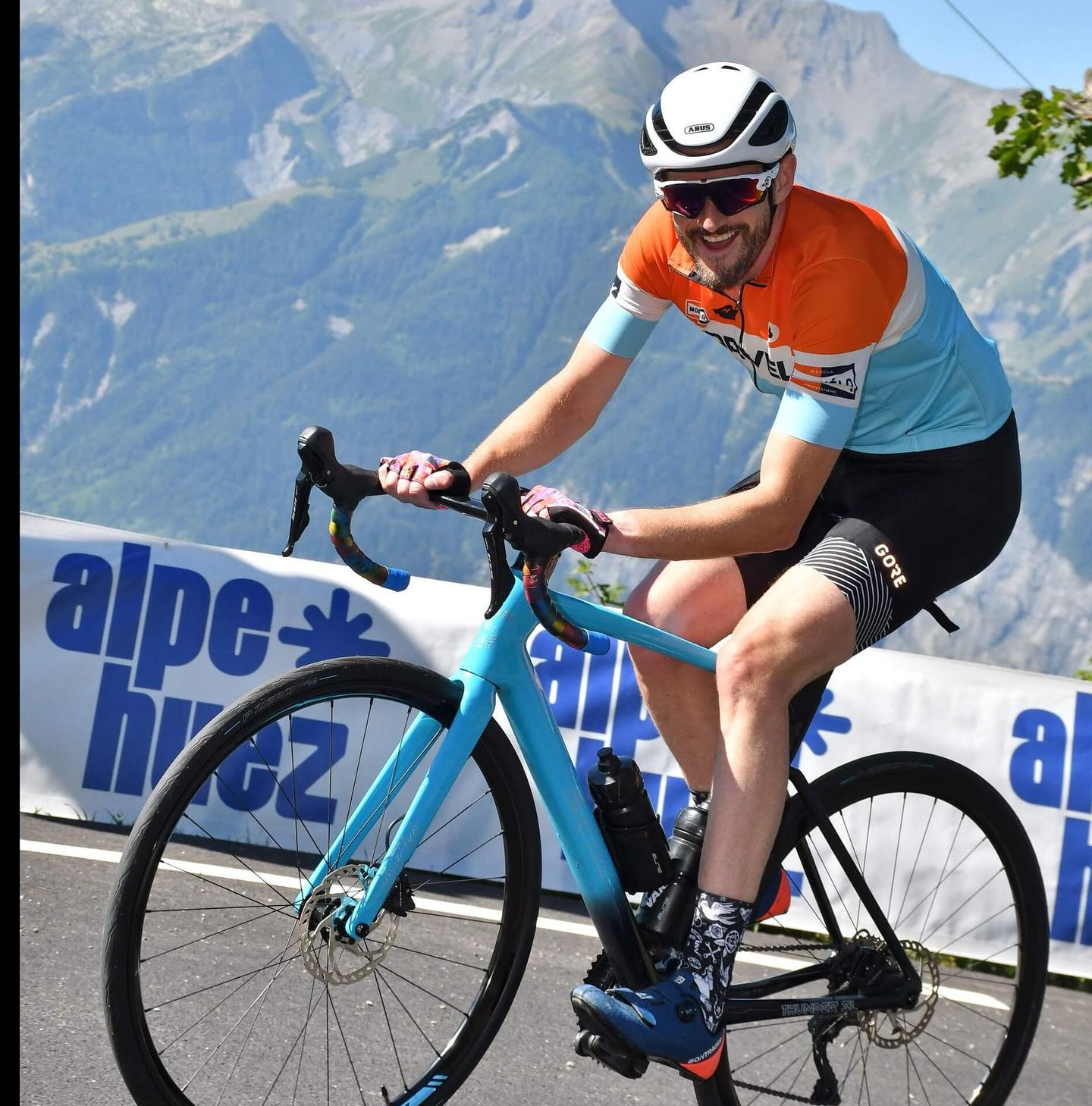 Joyful cyclist ascending Alpe d'Huez, clear blue skies and mountain scenery, cycling challenge in France