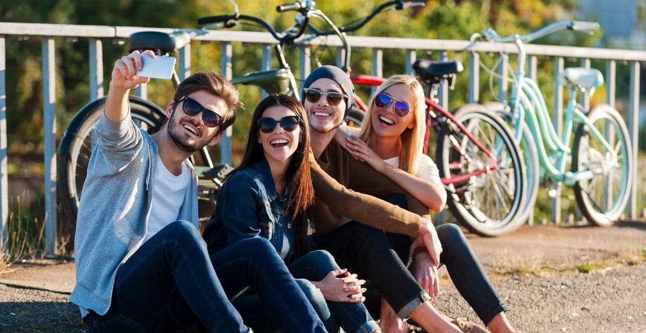 4 people sitting down by bikes taking a selfie