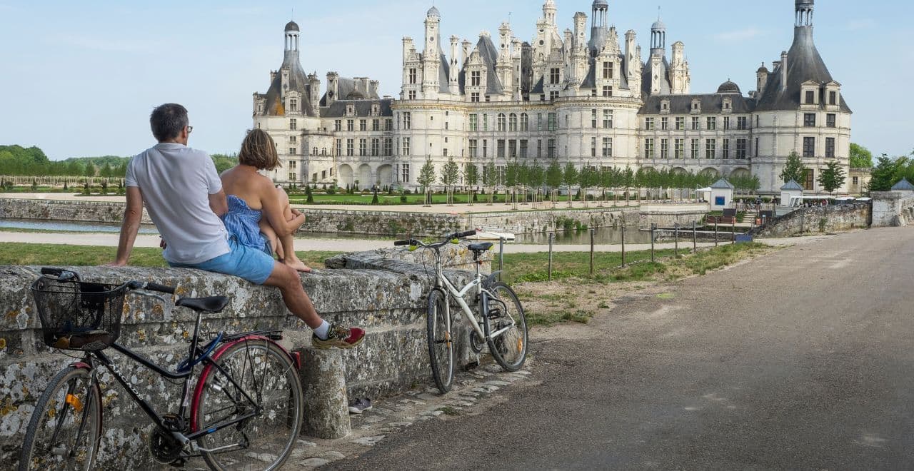 Couple sitting by their bikes, admiring Château de Chambord.