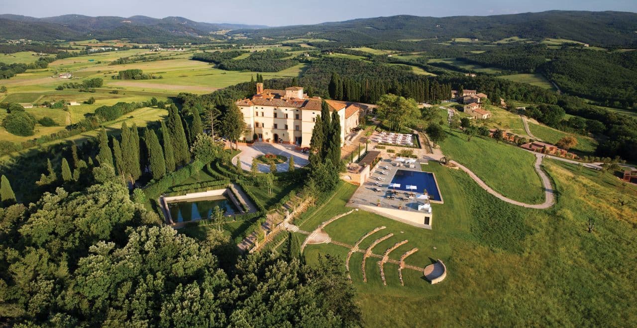 Aerial view of a hillside villa with surrounding greenery and pool