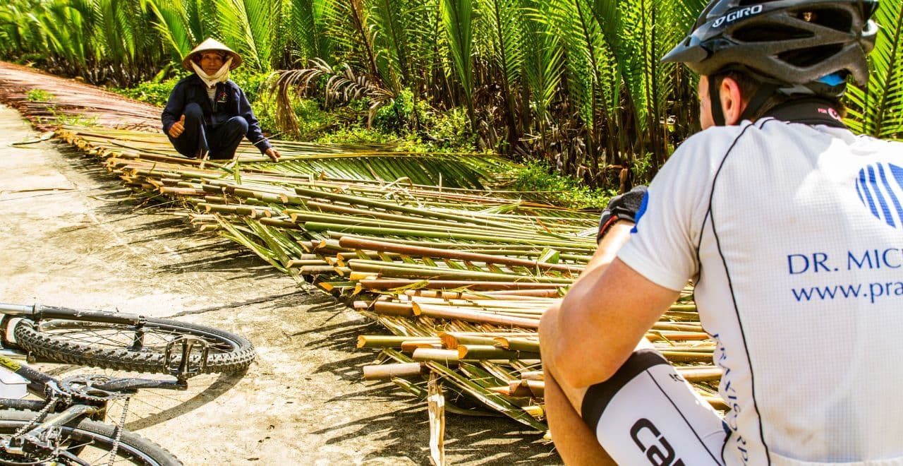 Cyclist watching a local worker harvest bamboo in Vietnam, blending cultural interaction with cycling exploration