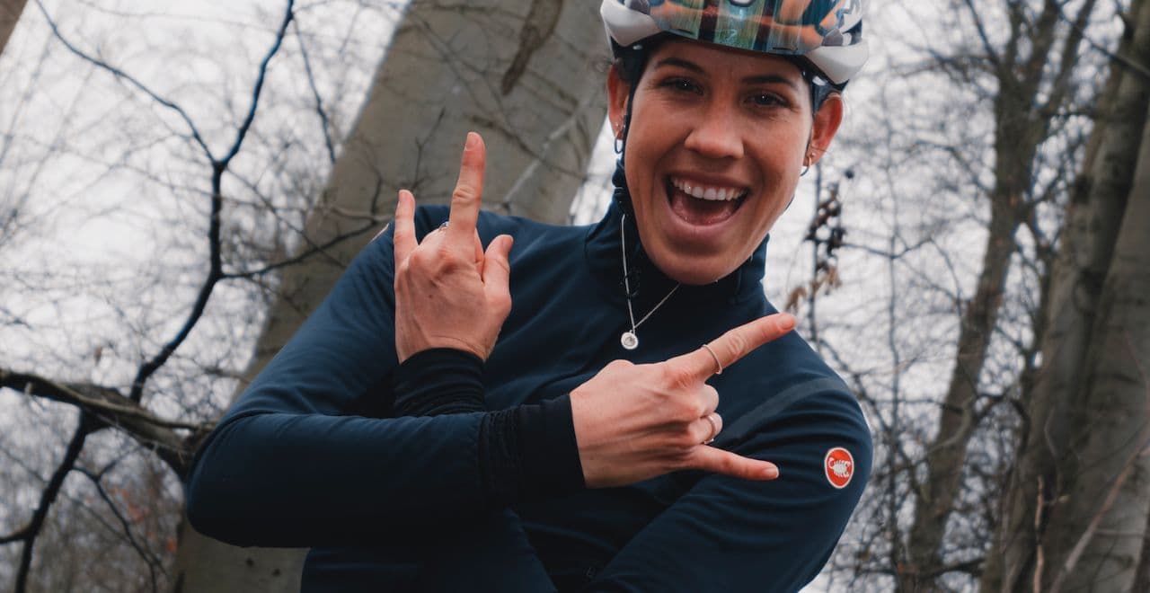 female cyclist in a forest smiling for the camera making a victory sign with her hands 