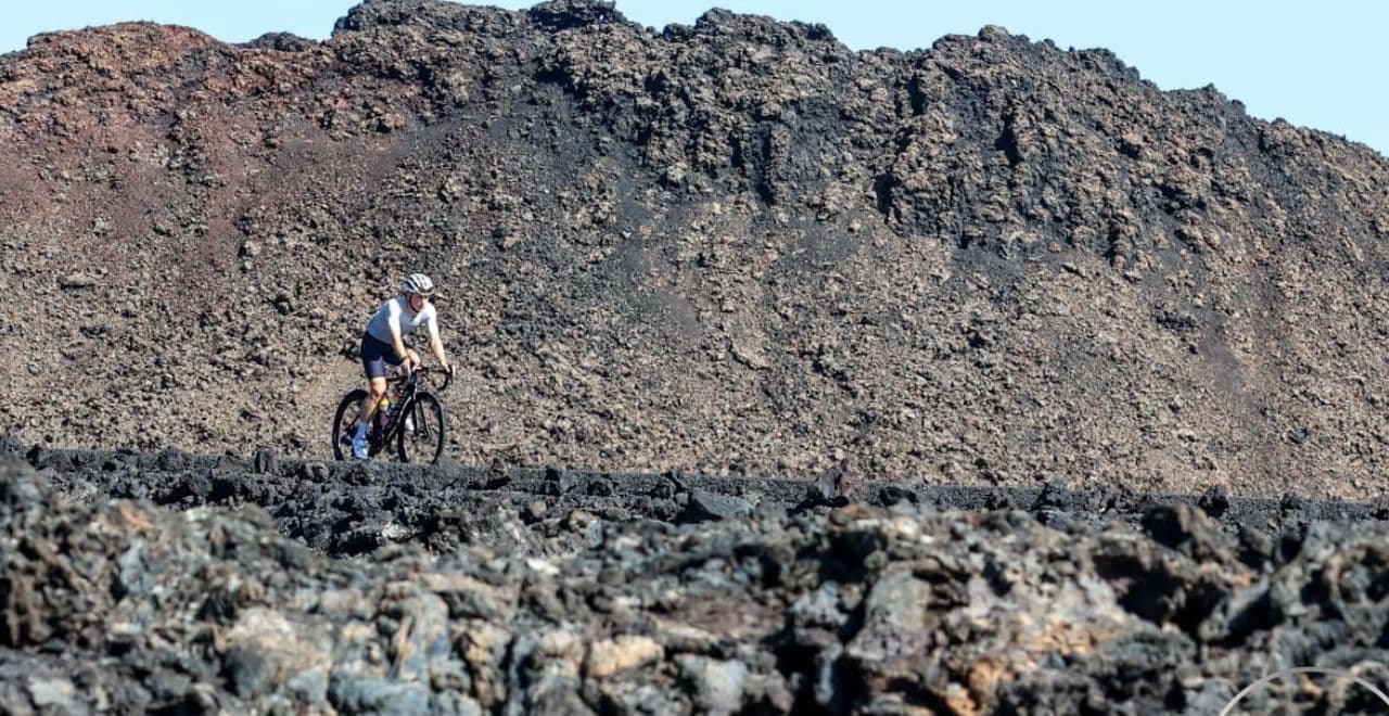 Cyclist riding through rugged volcanic terrain under clear sky