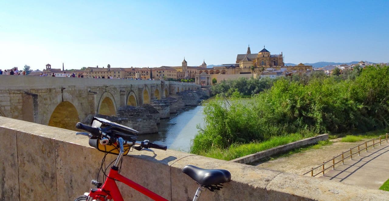 Red bicycle parked by Roman bridge with Córdoba’s Mosque-Cathedral view