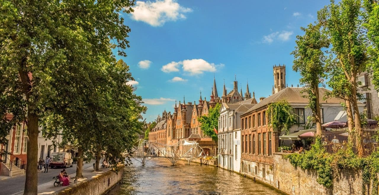 Medieval buildings along the canal with the Belfry of Bruges in the background.
