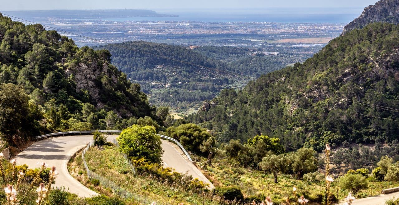 Curving mountain road with scenic views of lush hills and distant city.