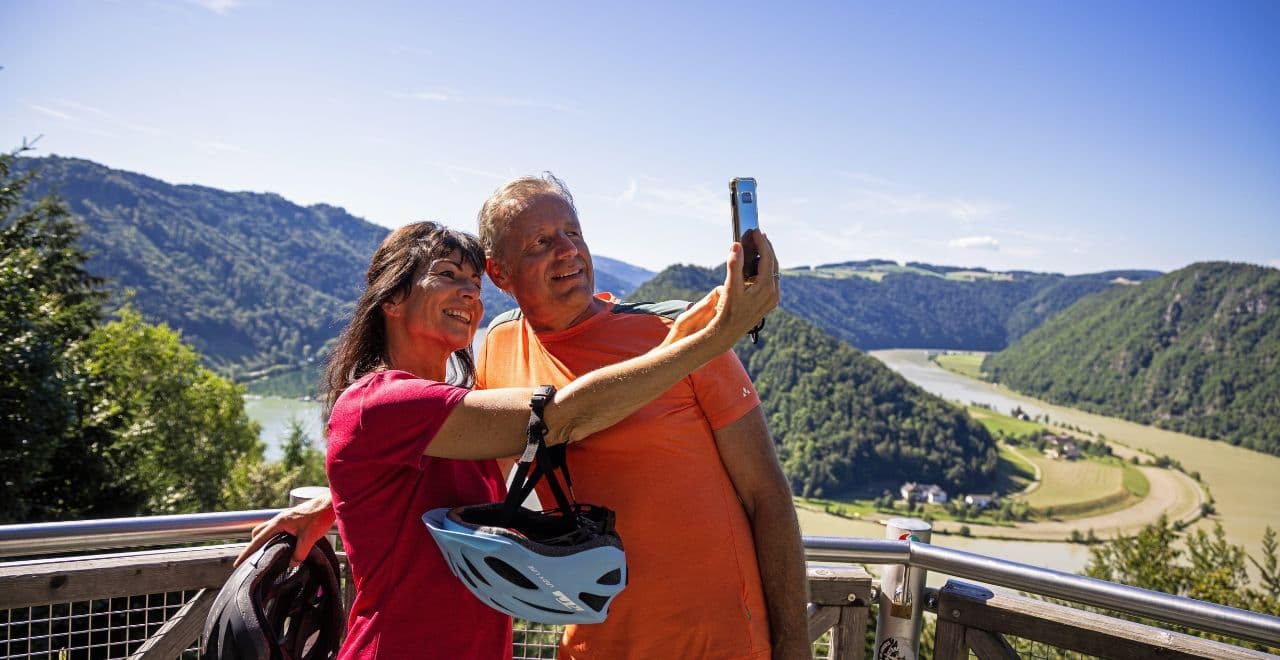 Couple taking a selfie at a scenic river viewpoint with lush hills
