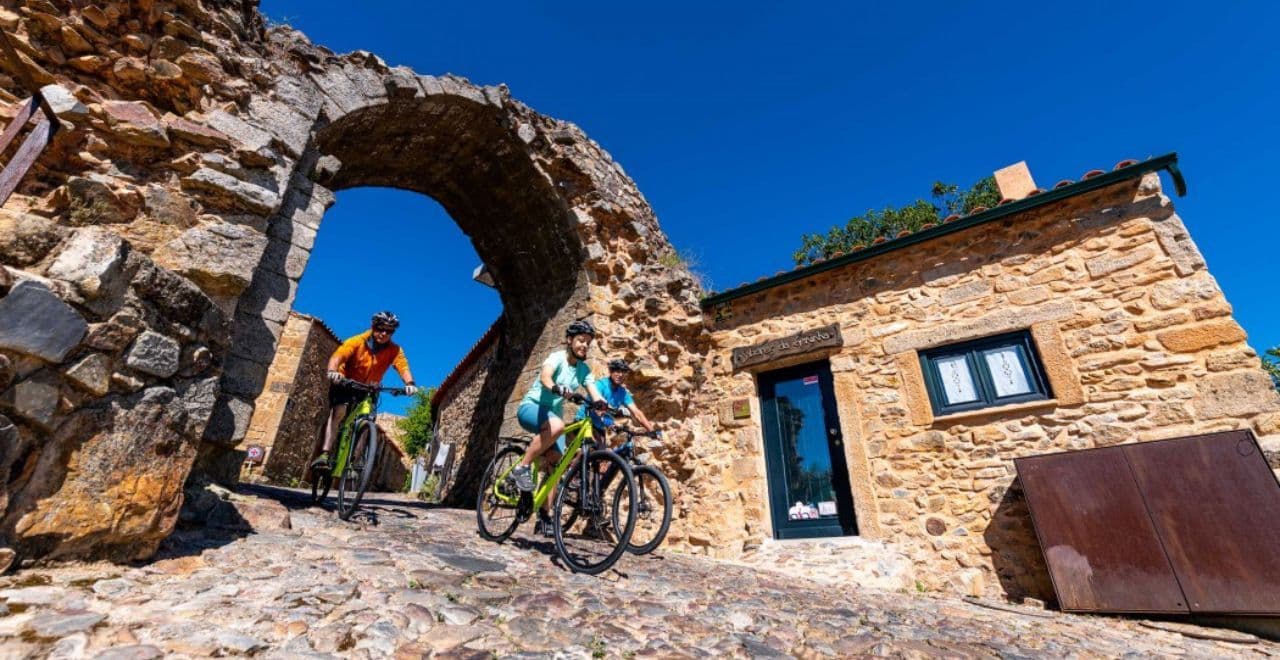 Cyclists passing through a historic stone arch in a rustic village